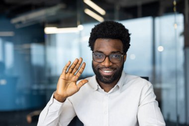 Parlak, modern bir ofiste otururken gözlük takan neşeli bir profesyonel. Bireyler, mesleki veya yaşam tarzı temaları için uygun olumluluk ve yaklaşımlarını ifade ederler.