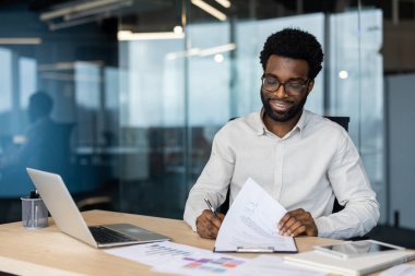 Ofis çalışanı, modern bir masada çalışırken verileri analiz ediyor ve evrak hazırlıyor..