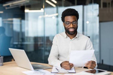 Ofiste profesyonel bir adam, belgeleri kontrol ediyor, modern teknolojiyle pozitif çalışma ortamı sergiliyor..