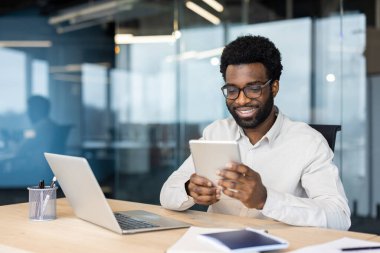 Çağdaş bir ofiste bilgisayarlı bir tablet kullanan erkek işçi, bir iş ortamında üretkenlik ve teknoloji sergiliyor, aynı zamanda profesyonellik yayıyor.