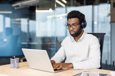 İş adamı kulaklığı açık görevlere odaklanıyor, çağdaş bir çalışma alanında dizüstü bilgisayar kullanıyor..