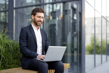 Modern bir ofisin dışında dizüstü bilgisayarda çalışan profesyonel bir adam, modern işleri gösteriyor..