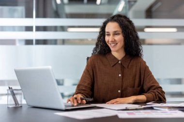 Kendine güvenen bir iş kadını şık bir ofis ortamında iş için dizüstü bilgisayar kullanıyor. Çevre, motivasyon, odaklanma ve başarıyı yansıtan üretken ve profesyonel bir atmosfer sergiliyor.