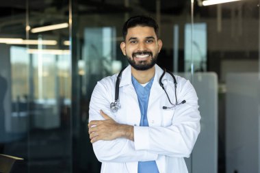 Profesyonel kıyafetli bir doktor modern bir klinikte dikilirken kendinden emin bir şekilde gülümser..