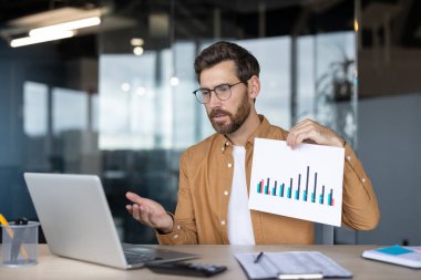 Ofisteki sanal bir toplantıda bar grafik raporunu sunan bir işadamı. Uzman, veri analizinde yer alıyor ve bir dizüstü bilgisayar kullanarak iş kavramlarının açıklamalarını yapıyor gibi görünüyor.