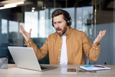 Ofis masasında dizüstü bilgisayarla kulaklık takan bir adam hayal kırıklığı yaşıyor..