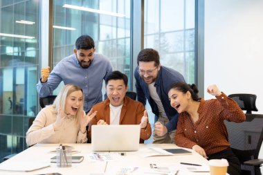 Beş profesyonelden oluşan bir grup, geniş pencereli çağdaş bir ofis ortamında dizüstü bilgisayar ekranına bakarken, takım çalışması, başarı ve kutlama yaparken keyif ve heyecan ifade ediyor..