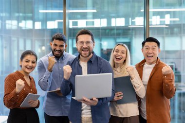 Bir grup meslektaş, profesyonel ofis ortamında coşku ve takım çalışması sergiliyor. Görüntü, modern bir şirket ortamında takım çalışması, iş başarıları ve işbirliği taşır..