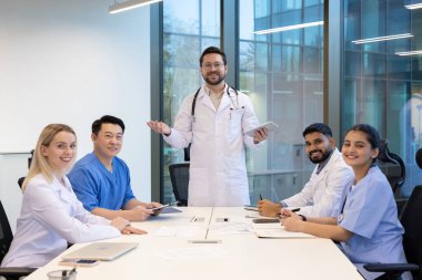 Çeşitli sağlık uzmanlarından oluşan bir grup, modern bir ofiste ortak bir tartışmaya girişerek, hasta bakımı ve organizasyonel iyileştirme stratejileri üzerinde fikir alışverişinde bulunmakta ve işbirliği yapmaktadır..