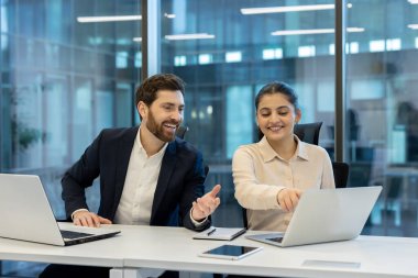 İki profesyonel iş arkadaşı, parlak bir ofiste fikirleri tartışırken dizüstü bilgisayar kullanıyorlar..