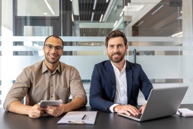 İki iş adamı birlikte oturmuş, planları tartışıyor ve fikirlerini paylaşıyorlar. Modern teknolojiyi çağdaş ofis ortamında kullanırken işbirliği, takım çalışması ve odaklanma iletiyorlar..