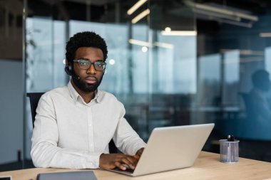 Kulaklık takan kendine güvenen bir müşteri hizmetleri temsilcisi, parlak, profesyonel ofis ortamında dizüstü bilgisayar kullanıyor, kendini adamışlığı, verimliliği ve mükemmel iletişim becerilerini yansıtıyor..