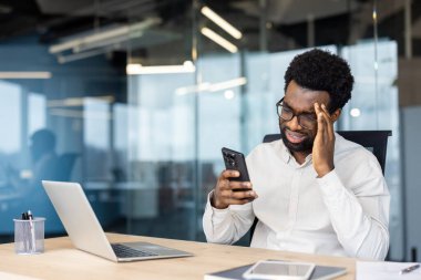Ofiste odaklanmış bir profesyonel akıllı telefonla iletişim kurarken stres yaratıyor. Laptop ve belgeler de dahil olmak üzere modern ofis ekipmanları