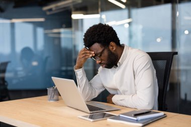 Ofis masasında dizüstü bilgisayarında çalışırken stresli görünen bir profesyonel, işyerindeki zorlukları ve verimlilik sorunlarını vurguluyor.