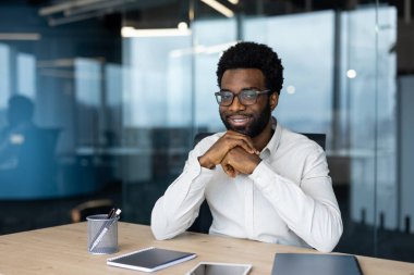 Modern ve parlak bir ofiste masa başında oturan kendine güvenen genç bir profesyonel. Atmosfer profesyonellik, üretkenlik ve pozitiflik hissi veriyor.
