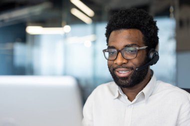Modern bir ofiste çalışan, kulaklık ve gözlük takan müşteri hizmetleri temsilcisi. İş ortamında dostane ve profesyonel iletişimi gösterir