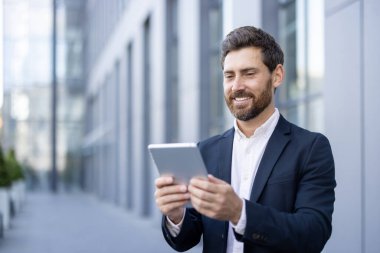 Açık havada tablet kullanan iş elbiseli bir adam, profesyonelliği ve modern çalışmaları aktarıyor..