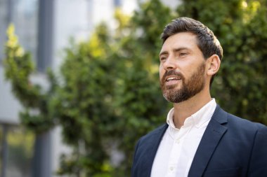 Kendine güveni olan bir adam, doğal yeşil bir geçmişi olan takım elbiseli açık havada duruyor..