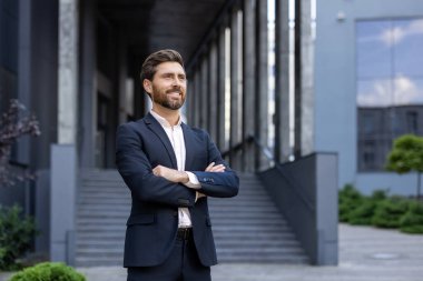 Modern bir binanın dışında kolları bağlı duran takım elbiseli profesyonel bir adam. İmaj, ticari ve profesyonel kavramlar için uygun bir güven, başarı ve liderlik duygusu taşır..