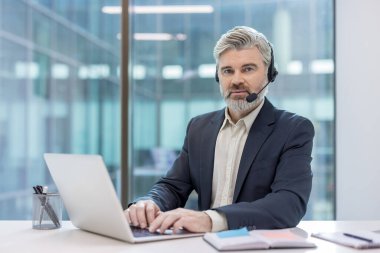 İşletme profesyoneli uzaktan bilgisayar ve kulaklık kullanarak hizmet veriyor. Modern görünümlü ve etkili iletişim odaklı ofis ortamı.