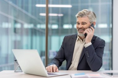 Üst düzey bir profesyonel bir telefon görüşmesi yaptı, modern ofis ortamında bilgisayarının başında çalışıyor, profesyonelliği, teknolojiyi ve iletişimi sergiliyor..