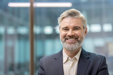 Gri sakallı, profesyonel bir ofis ortamında gülen olgun bir iş adamı..