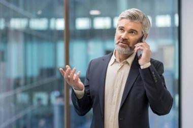 Takım elbiseli kendine güvenen bir adam, çağdaş bir ofis ortamında telefonla konuşuyor..