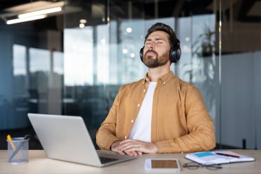 Ofis çalışanı kapalı gözlerle müziğin keyfini çıkarıyor, masasındaki görevlere hak ettiği kadar ara veriyor, bir dizüstü bilgisayar, tablet ve not defteri ile çevrili, rahatlama ve sükuneti kucaklıyor.