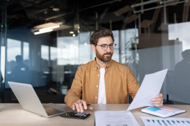 Finansal belgeleri incelerken, bütçeleri yönetirken ve modern ofis ortamında verileri analiz ederken, bir hesap makinesi kullanarak özenle çalışan bir muhasebeci