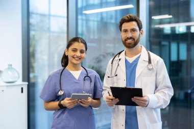 Doktor ve hemşire, modern hastane ortamında dijital tablet ve pano tutarken gülümsüyor, ekip çalışması ve ileri tıbbi teknoloji sergiliyor.