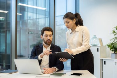 İki iş arkadaşı, verileri gözden geçirmek ve modern ofis ortamında stratejileri tartışmak, takım çalışması ve üretkenliği teşvik etmek amacıyla bir dizüstü bilgisayar ve pano kullanarak bir proje üzerinde işbirliği yapıyorlar.