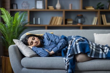 Young Muslim woman resting and sleeping at home on the sofa covered with a blanket.