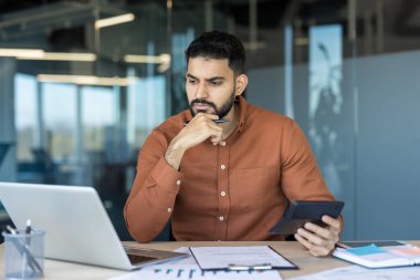 Thoughtful business person analyzing financial data, calculating budget costs with a calculator and laptop, working diligently on important accounting tasks in a modern office