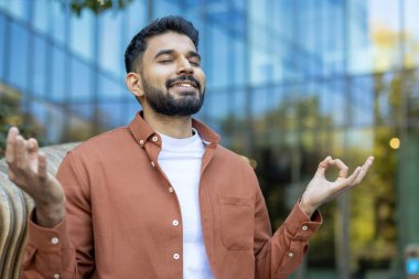 Indian man meditating zen-style outdoors, keeping eyes closed, focusing on breath, and practicing mindfulness for mental balance and emotional well-being