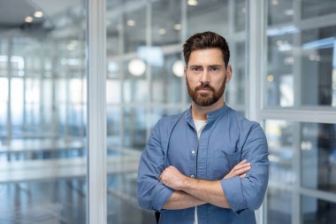 Confident bearded man with arms crossed in a modern office, projecting professionalism, leadership and determination as a successful executive or entrepreneur in a corporate workspace