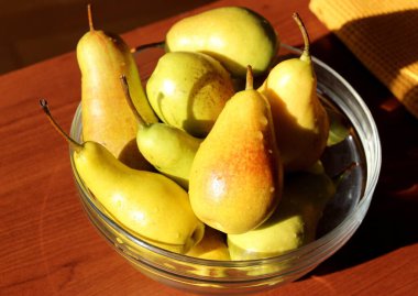 Masadaki şeffaf cam kasede olgun sarı-yeşil armutlar..