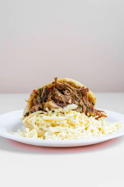 Beyaz tabakta et ve peynirle doldurulmuş arepa.