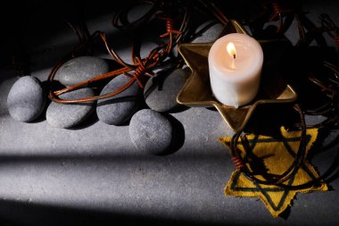 Holocaust memory day. Barbed wire, stones, yellow star and burning candle on black background. High quality photo