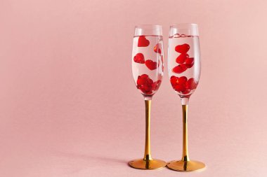 Happy Valentines Day. Two glasses of champagne wine with red hearts in them. Pink background