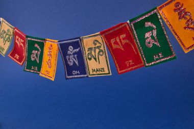 Tibetan Buddhist flags against blue background with copy space. Text on flags Om mani padme hum meaning The jewel is in the lotus.
