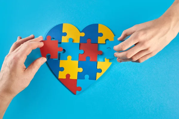 Father and autistic son hands holding jigsaw puzzle heart shape. Autism spectrum disorder family support concept. World Autism Awareness Day.