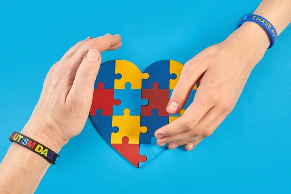 Father and autistic son hands holding jigsaw puzzle heart shape. Autism spectrum disorder family support concept. World Autism Awareness Day.