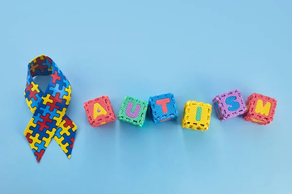Word Autism Awareness day. Autism Awareness Ribbon and Puzzle cubes on blue background