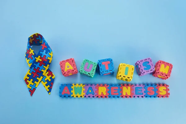 Word Autism Awareness day. Autism Awareness Ribbon and Puzzle cubes on blue background