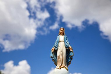 Mary 'nin varsayımı. Beyaz bulutlu mavi gökyüzü ile Bakire Meryem heykeli