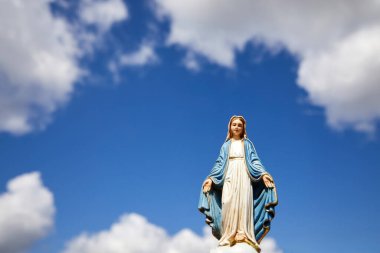 Mary 'nin varsayımı. Beyaz bulutlu mavi gökyüzü ile Bakire Meryem heykeli