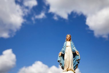 Mary 'nin varsayımı. Beyaz bulutlu mavi gökyüzü ile Bakire Meryem heykeli