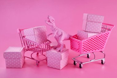 Pembe Cuma konsepti. Pembe arka planda hediye kutularıyla dolu alışveriş arabası olan komik pembe dinozor oyuncağı..