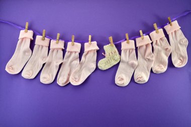World Prematurity day concept. Normal size and tiny socks on rope on purple background. clipart
