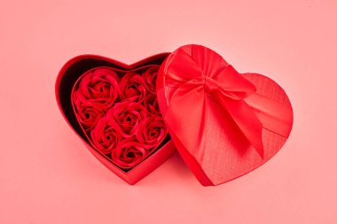 Kalp şeklinde hediye kutusu, pembe arka planda Sevgililer Günü için güller..